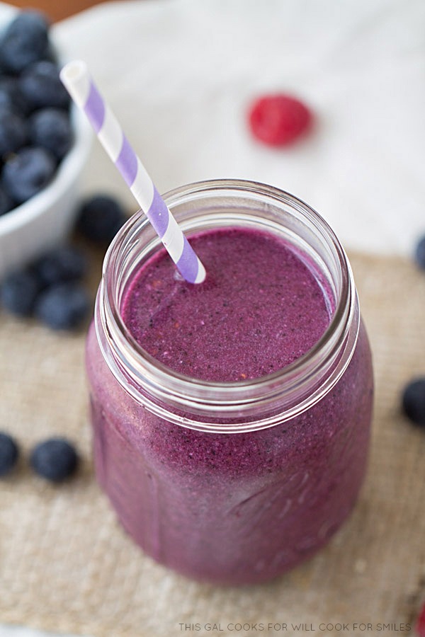 berry smoothy in a mason jar and a bowl of blueberries to the left 